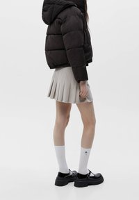 Svart puffjacka, plisserad beige kjol, vita strumpor med ett blått manetmönster och svarta plattform Mary Jane-skor.