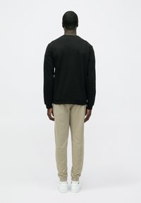 Čierna mikina s rebrovanými manžetami a lemom, doplnená svetlobéžovými teplákmi a bielymi teniskami, pohľad zozadu.