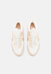 Pari valkoisia ja beigejä Nike-juoksukenkiä, näkönä ylhäältä, joissa on nauhat ja Nike-swoosh-logo sivuilla ja pohjilla.