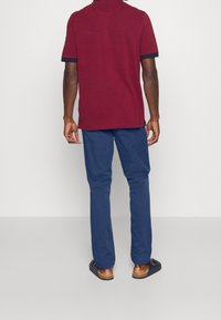 Burgundy pikétröja med marinblå kanter, ihop med blå byxor. Outfiten har en avslappnad passform och kompletteras av bruna slip-on skor.