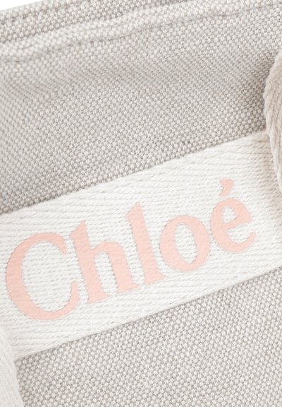 Tessuto telato beige con una finitura testurizzata, caratterizzato da un'etichetta bianca con il logo "Chloé" in lettere rosa chiaro.