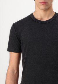 Sort bomulds T-shirt med rund halsudskæring og korte ærmer. Har en glat tekstur og minimal syning langs kraven.