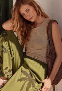 Tan ribbet top kombineret med løse olivengrønne bukser med et palmebladsdesign. Brun hæklet taske tilføjer tekstur til outfittet.