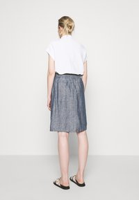 White short-sleeve top with a high neckline paired with a blue denim skirt featuring an elastic waistband and a side slit.