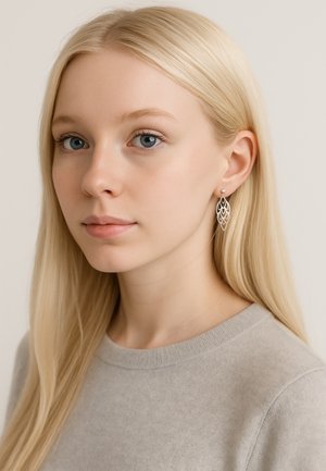 Söderbladsformat silverörhängen med intrikata utskärningar, prydda med en liten pärla, bärs av en person med långt blont hår.