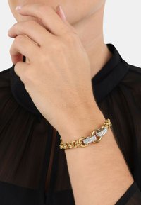 Pulsera de cadena de oro con eslabones entrelazados, acentos texturizados y dos segmentos brillantes adornados con cristales claros.