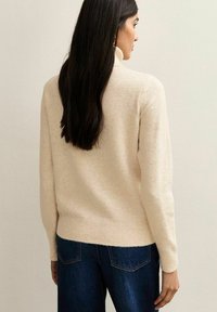 Crème-kleurige trui met een geribde zoom en manchetten, zachte textuur, ronde halslijn en een relaxed fit, gecombineerd met donkerblauwe jeans.