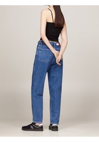 Jeansy z wysokim stanem w niebieskim kolorze, luźny krój, pięć kieszeni i biała oraz czerwona metka z tyłu. Połączone z czarnymi trampkami.