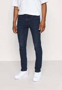 Mörkblå slim-fit jeans i denimtyg, med medelhög midja, klassisk femficksdesign och subtila blekningar. Bärs med vita sneakers.