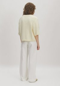 Gelbes, strukturiertes Kurzarmoberteil mit rundem Ausschnitt, kombiniert mit locker sitzenden weißen Hosen. Schlichtes Design, keine sichtbaren Muster.