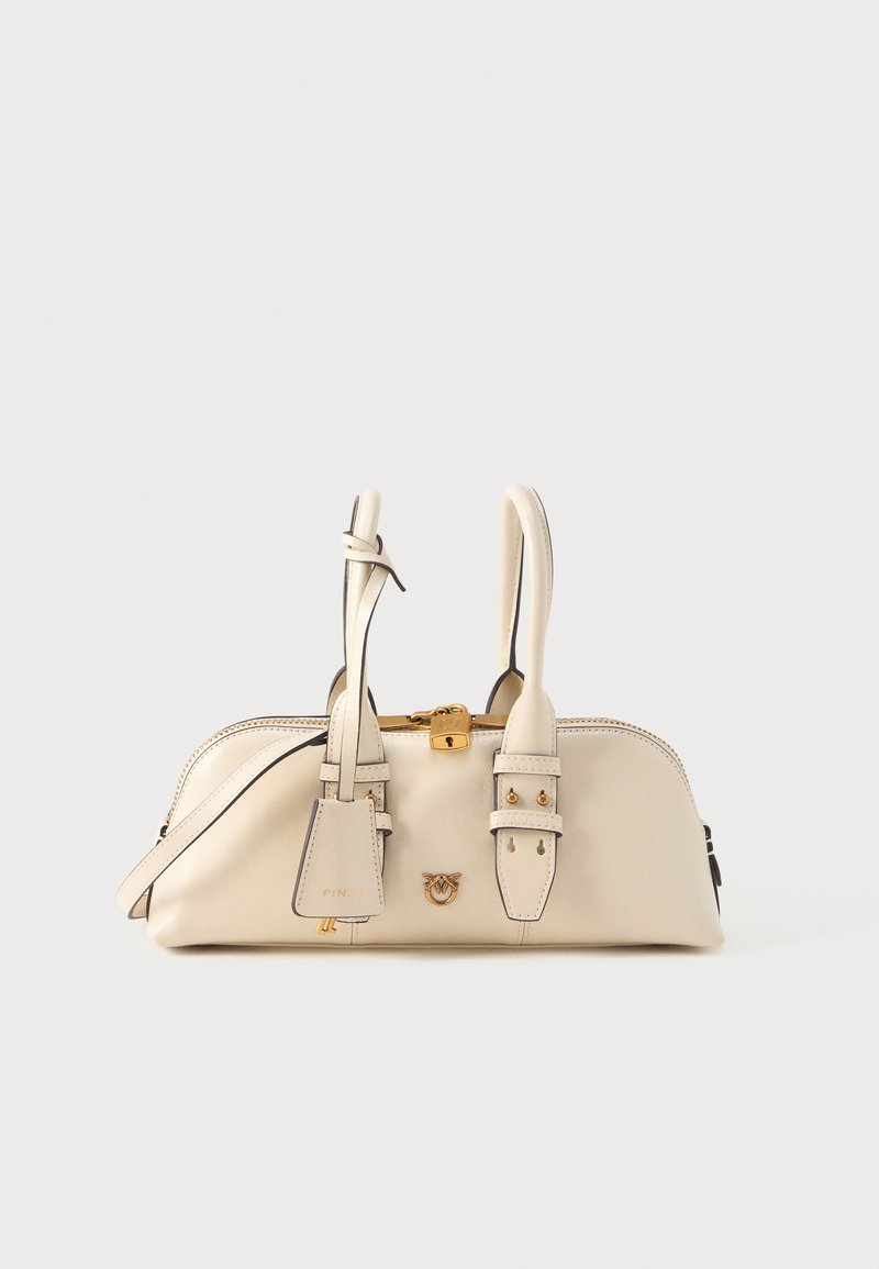 Krém színű bőr kézitáska dupla fogantyúkkal, arany zárakkal és logó részlettel, valamint egy kis fityegő címkével sima fehér háttéren.