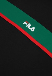 Un tejido negro presenta una banda a rayas verde y roja con el logo "FILA" en blanco. El material es suave; el diseño es elegante y moderno.