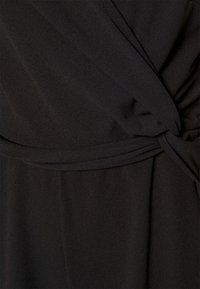 Černá látka s měkkou texturou má na pase detail ve tvaru zkrouceného uzlu a hladký splývavý design.