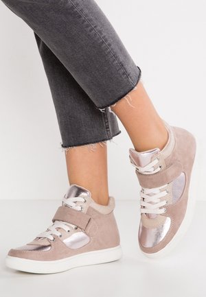 Alastomat jalat, joissa on lyhyeksi leikatut mustat farkut ja beiget korkeavartiset tennarit, joissa on metallinhohtoiset vaaleanpunaiset paneelit ja valkoiset pohjat.