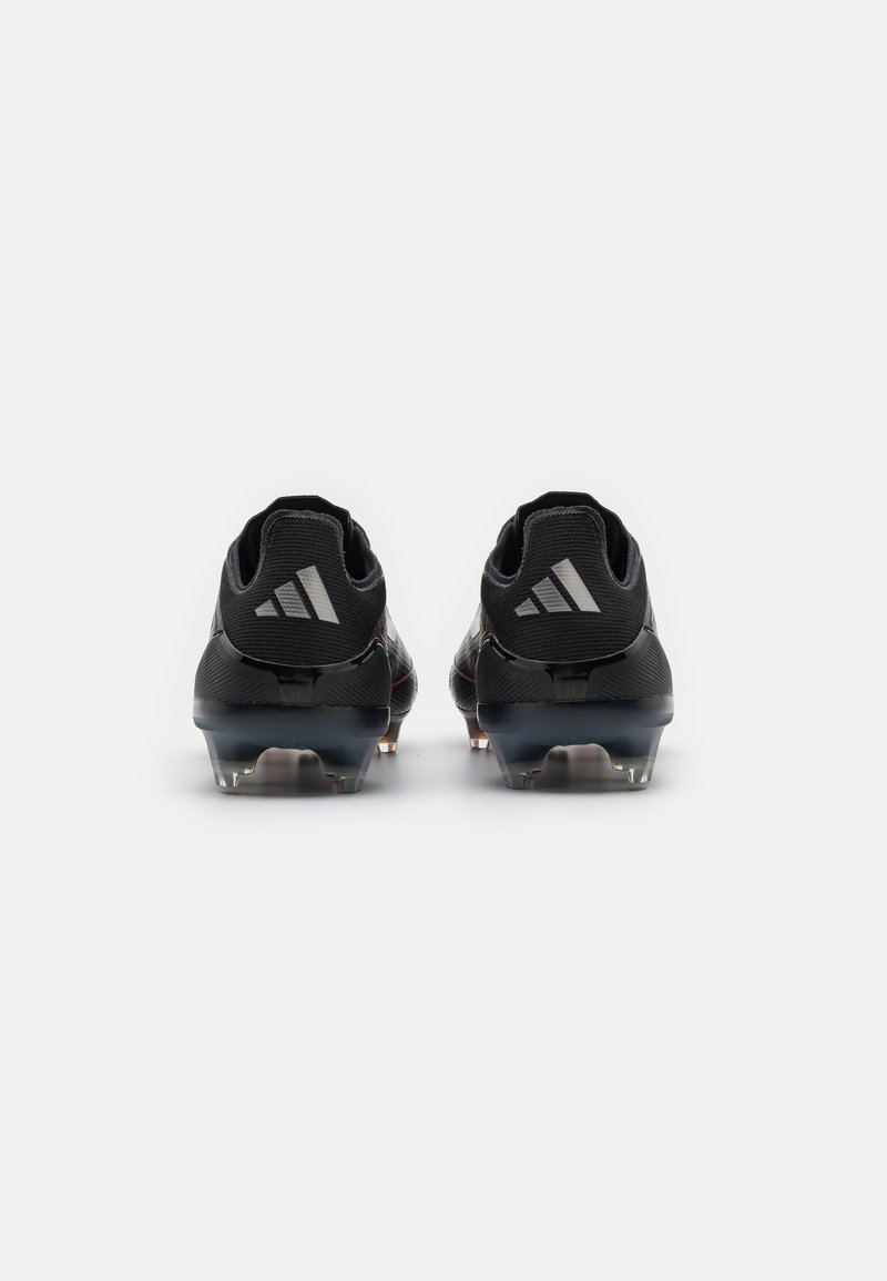 Botas de fútbol negras con upper sintético texturizado, soporte en el talón y tacos transparentes. Presenta tres rayas blancas en el talón.