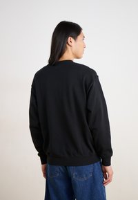 Sudadera negra con escote redondo, corte holgado, puños y dobladillo de canalé. Presenta una textura suave y un diseño minimalista, combinada con jeans azules.