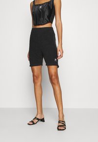 Svarta handduksshorts med en mjuk textur och rå kant, med en broderad logotyp på vänster ben och sidofickor. Kombineras med en svart crop top.