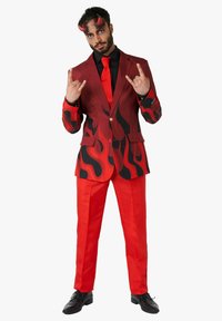 Traje de cuadros rojo y negro con motivos de llamas, combinado con una corbata roja y una camisa negra. El modelo lleva zapatos de vestir negros y posa con señales de mano.