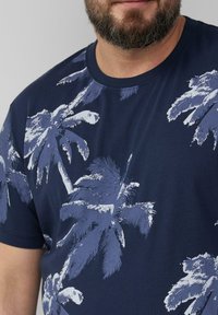 Granatowa koszulka z krótkim rękawem z nadrukiem palmy w jasnym niebieskim kolorze. Klasyczny okrągły dekolt i miękka tekstura bawełnianego materiału.