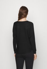 Svart stickad tröja med en texturerad design, långa ärmar och bred rund halsringning. Rundad fåll och åtsittande ärmslut.