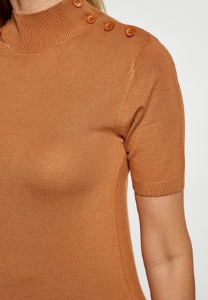 Kortærmet sweater med høj hals i lys brun strikket stof; har ribbet tekstur og fire knapdetaljer på skulderen.