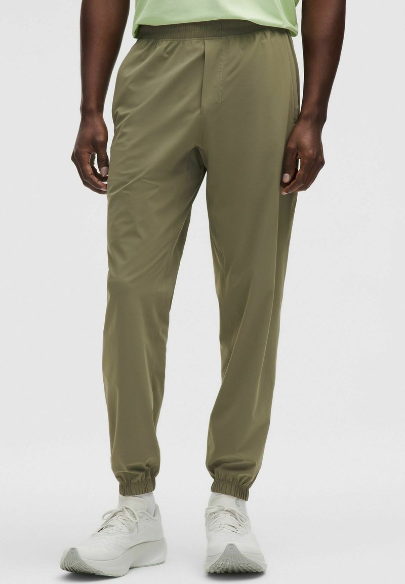 Joggers ligeros en verde oliva con cinturilla y puños elásticos. La tela suave con bolsillos laterales mejora la practicidad. Combinados con zapatillas blancas.