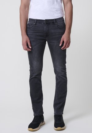 Jeans de mezclilla oscuros de corte slim con un lavado desgastado, que cuentan con cinco bolsillos y cierre de cremallera. Combinados con zapatillas negras y una camiseta blanca sencilla.