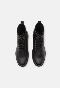 Botas de cuero negro hasta el tobillo con punta redonda, diseño de cordones, costuras en contraste y tirador en el talón para facilitar su uso.