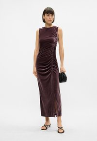 Μωβ αμάνικο φόρεμα με βελούδινη υφή, λεπτομέρεια πτυχών στο πλάι και ψηλή σχισμή. Συνδυάζεται με μια μικρή μαύρη τσάντα και σανδάλια με λουριά.