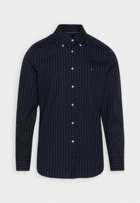 Navyblauwe langemouwen knoopshirt met witte stippen en een knoopkraag, tentoongesteld op een witte achtergrond.