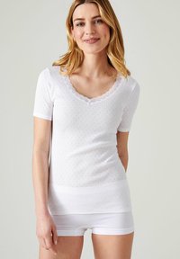 Witte korte mouwen top met een geschulpte V-hals, textuurstof met kleine oogjes patroon, gecombineerd met witte onderkleding.