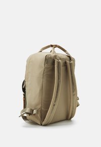 Beige backpack with padded straps, a top handle, and a smooth fabric texture. Features side pocket and adjustable straps for comfort.