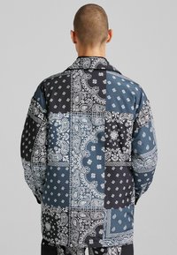 Lappad skjorta med bandanamönster i svart och blå toner, med kontrasterande texturer och en avslappnad passform.