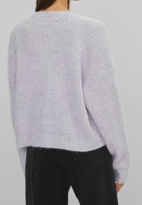 Lyse lilla strikket sweater med løs pasform, faldende skuldre og ribbet tekstur. Har en rund halsudskæring og rå kant.