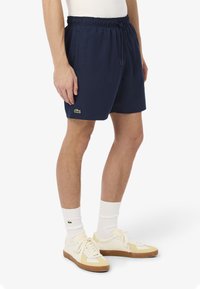 Pantaloni da bagno blu navy realizzati in materiale leggero, con vita elastica, cordoncino e un accento di logo verde sull'orlo.