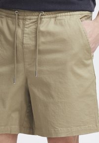 Shorts kaki en tissu doux, avec une ceinture élastique à cordon, des poches latérales et une coupe décontractée.