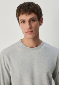 Hellgraues, geripptes Langarmshirt mit Rundhalsausschnitt. Weiche Textur, schlichtes Design, ohne sichtbare Muster oder Akzente.