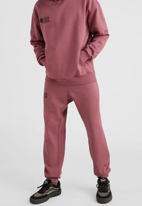 Sudadera rosa y joggers a juego hechos de tela suave. Presenta un logo en el pecho y en el muslo, con puños y cintura elásticos.