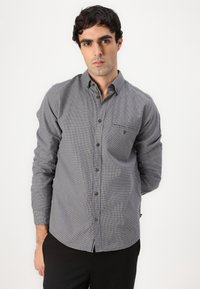 Gray and white checkered button-up shirt with a chest pocket, long sleeves, and a rounded hem. Fabric has a subtle texture.