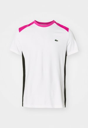 Camiseta blanca con acentos rosas en los hombros y paneles laterales negros. Cuenta con un pequeño logo bordado en verde en el pecho. Mangas cortas, corte clásico.