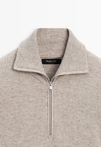 Maglione beige a coste con mezza cerniera e collo alto, caratterizzato da una cerniera argentata e un'etichetta con la scritta "Massimo Dutti". Tessuto morbido a maglia.