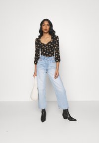 Sort blomster bodysuit med puffærmer, lyseblå lige jeans og sorte ankelstøvler. Modellen holder en hvid tekstureret taske.