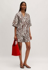 Bruine en witte zebra-patroon shirt en short set gemaakt van lichtgewicht stof, gecombineerd met een rode boodschappentas. Platte zwarte sandalen gedragen.