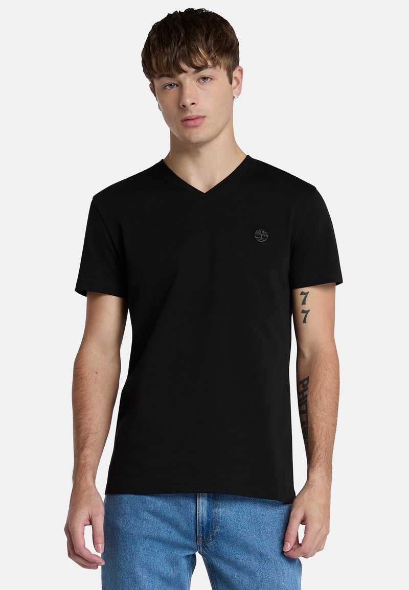Maglietta nera a V in cotone, con maniche corte e un piccolo logo sul petto. Abbinata a jeans in denim blu chiaro.