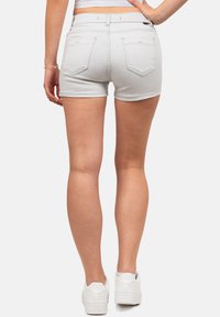 Shorts en denim gris clair avec un design ajusté, dotés de poches arrière et d'un ourlet roulé. Associés à des baskets blanches.