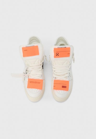 Αθλητικά παπούτσια υψηλής γλώσσας από λευκό δέρμα, με ζωηρές πορτοκαλί ετικέτες, επίπεδα κορδόνια, διάτρητο μπροστινό μέρος και υφασμένα λαστιχένια πέλματα.