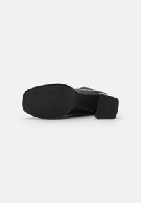 Suela de zapato para hombre en negro con una superficie de goma texturizada, puntera redondeada y un tacón resistente con marca antideslizante en relieve.