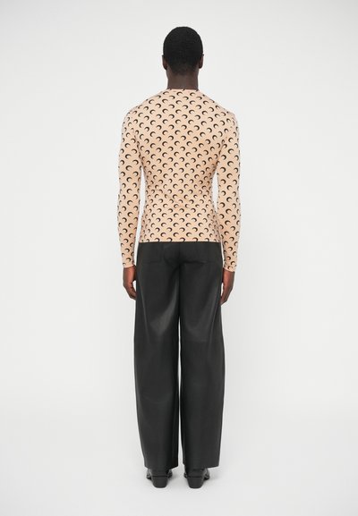 Világos barack színű, hosszú ujjú, testhez simuló felső, fekete félhold mintával ismételve, bő fekete nadrággal párosítva, a modell hátulról látható.