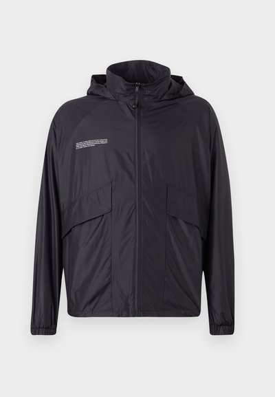 Lightweight black jacket with a zip front, hood, and large side pockets. Made of smooth, water-resistant material, featuring subtle text detail.