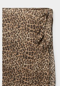 Tissu en imprimé léopard avec des taches irrégulières brun, beige et noir, plié avec un nœud lâche à un coin.